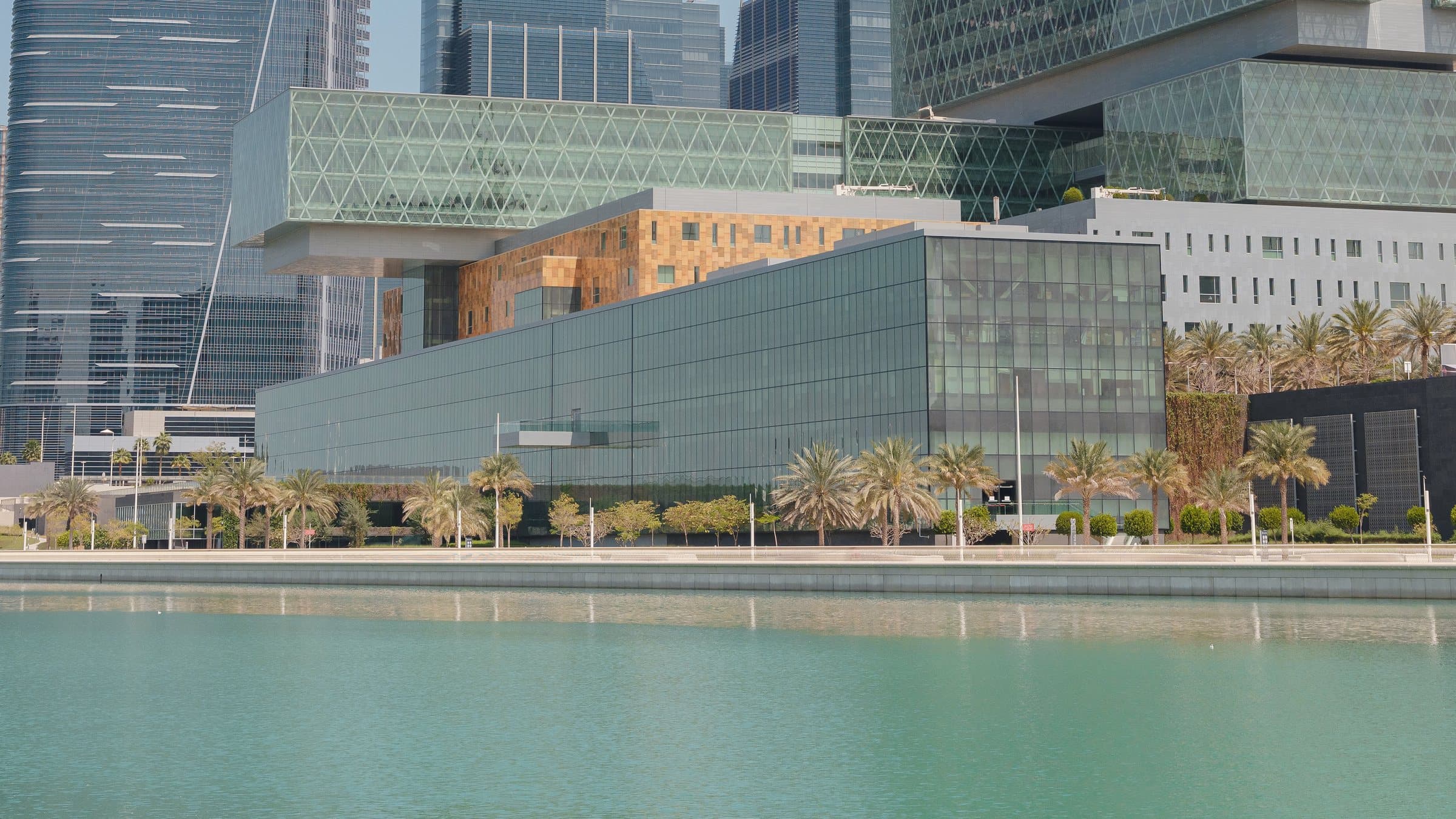 Modern glass buildings and palm trees along the waterfront of Al Maryah Island, Abu Dhabi.